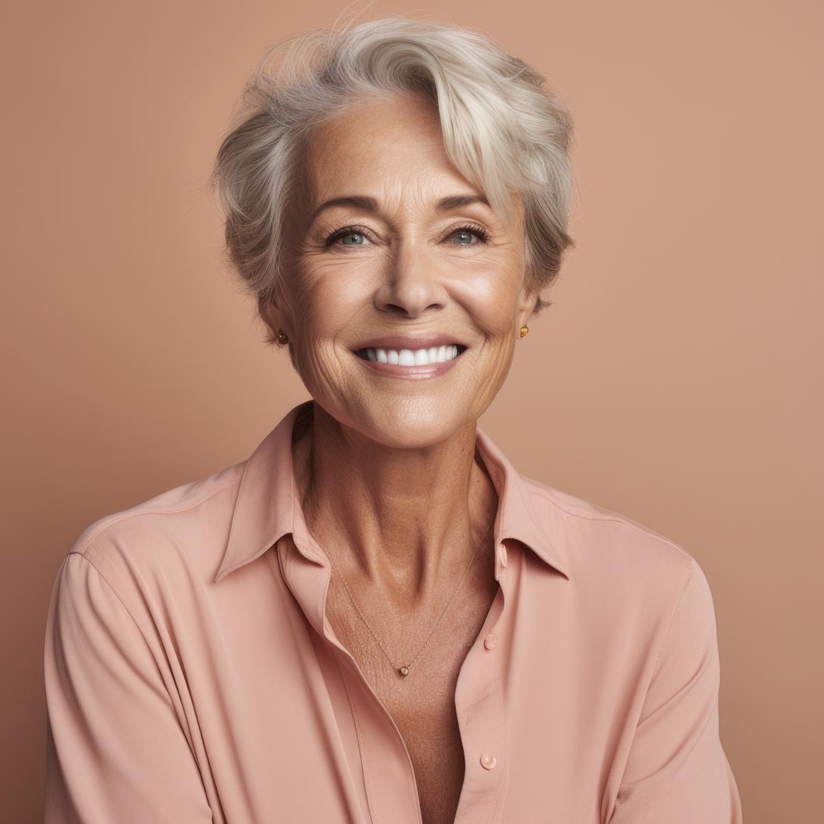 Confident senior woman with short silver hair smiling in a peach-colored blouse, radiating health and elegance against a neutral background.