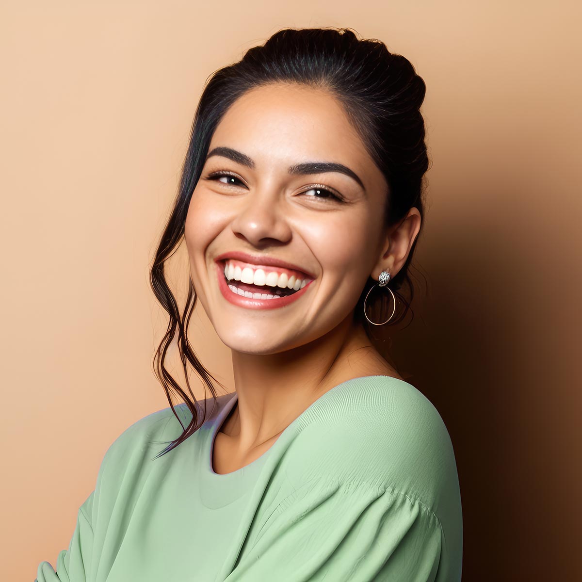 Smiling young woman with dark hair wearing a light green top, radiating confidence and joy against a neutral background.