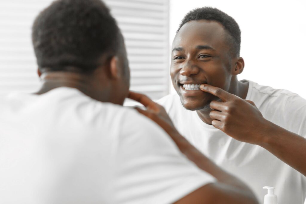 Smiling man examining his teeth in the mirror, highlighting good oral hygiene and dental care practices.