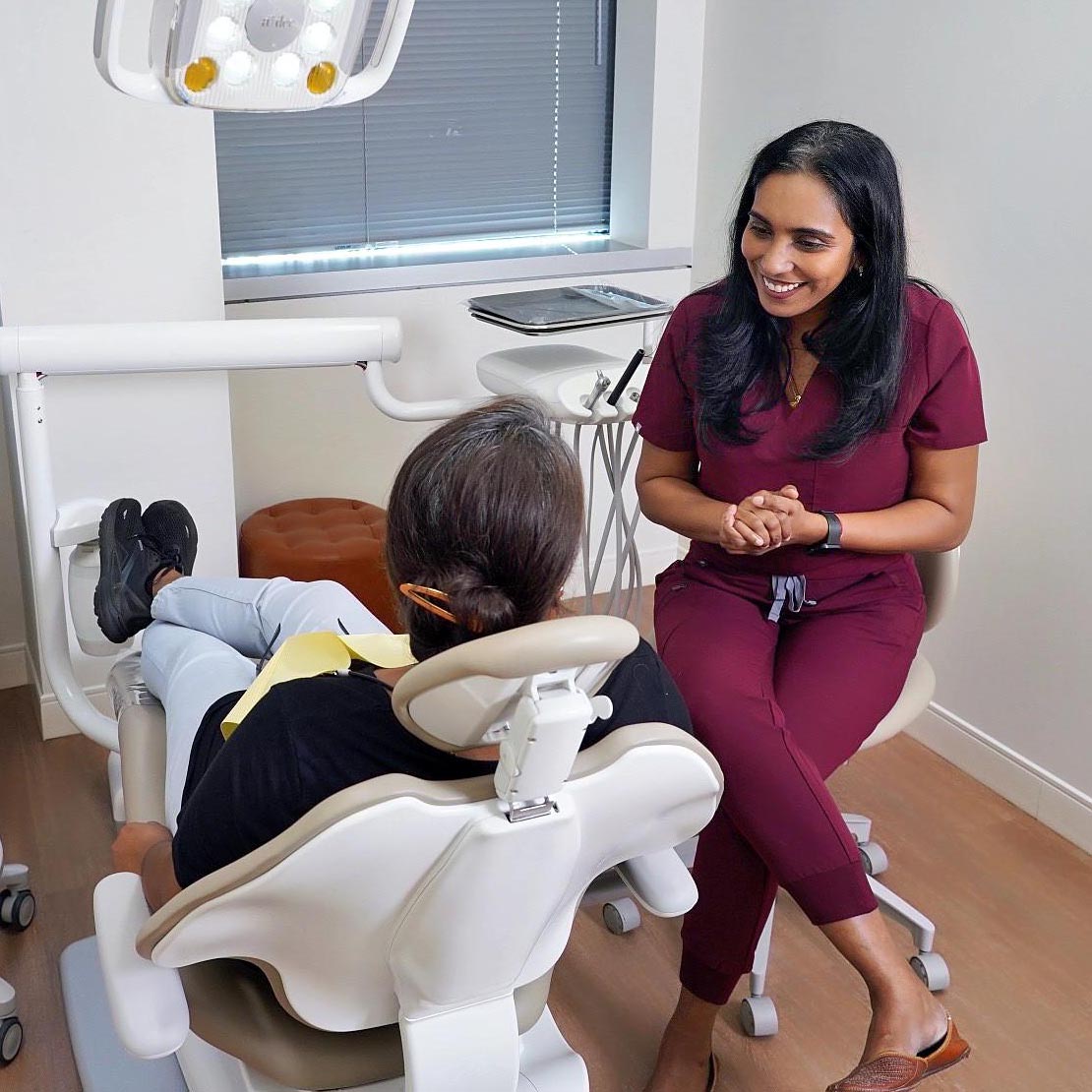 Dr. Archana Srinivasan smiling to her patient sitting on dental chair's third view.