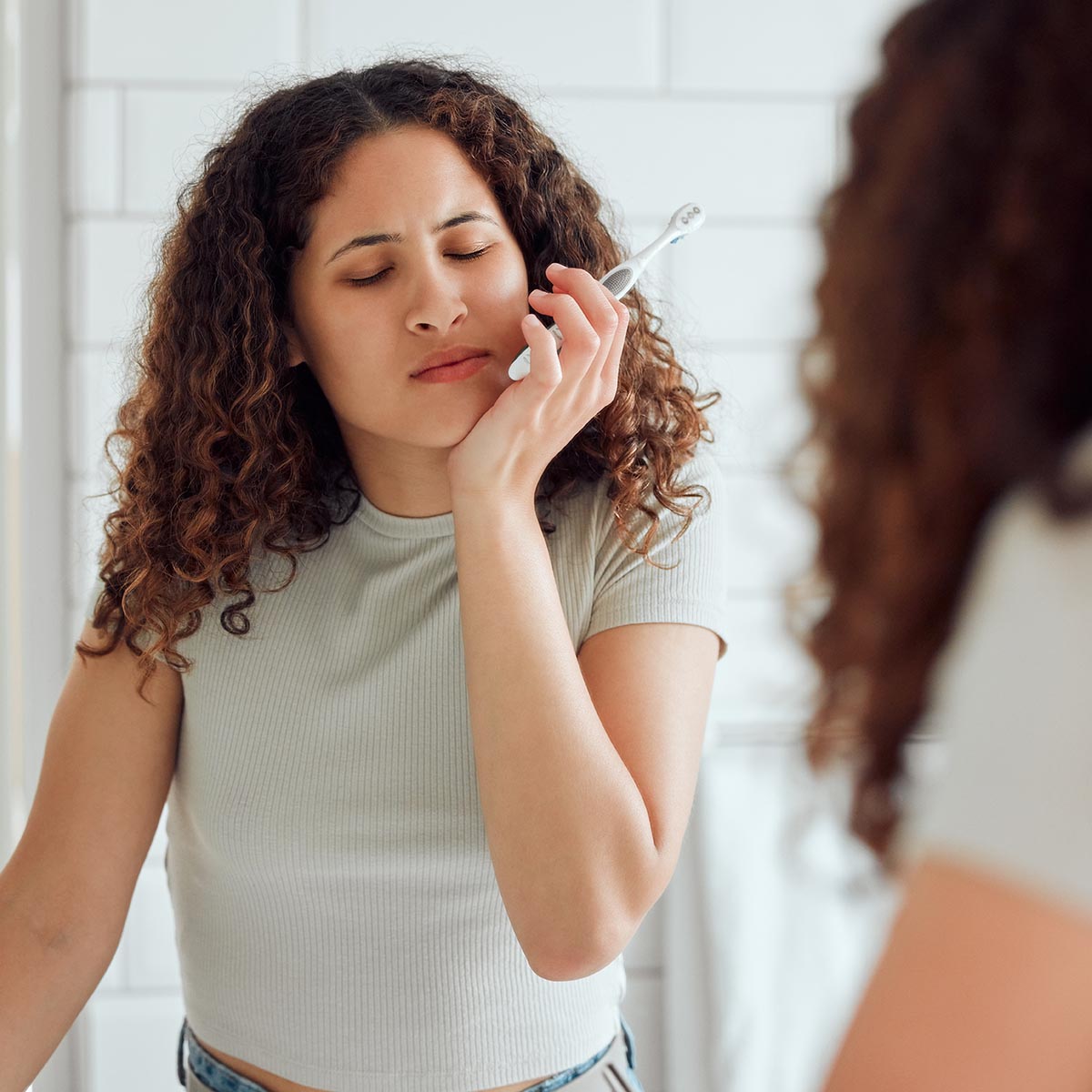 Toothache, oral pain and dental sensitivity for a woman brushing her teeth in the morning. African American female suffering with a painful, hurting or inflammation in her mouth in the bathroom.